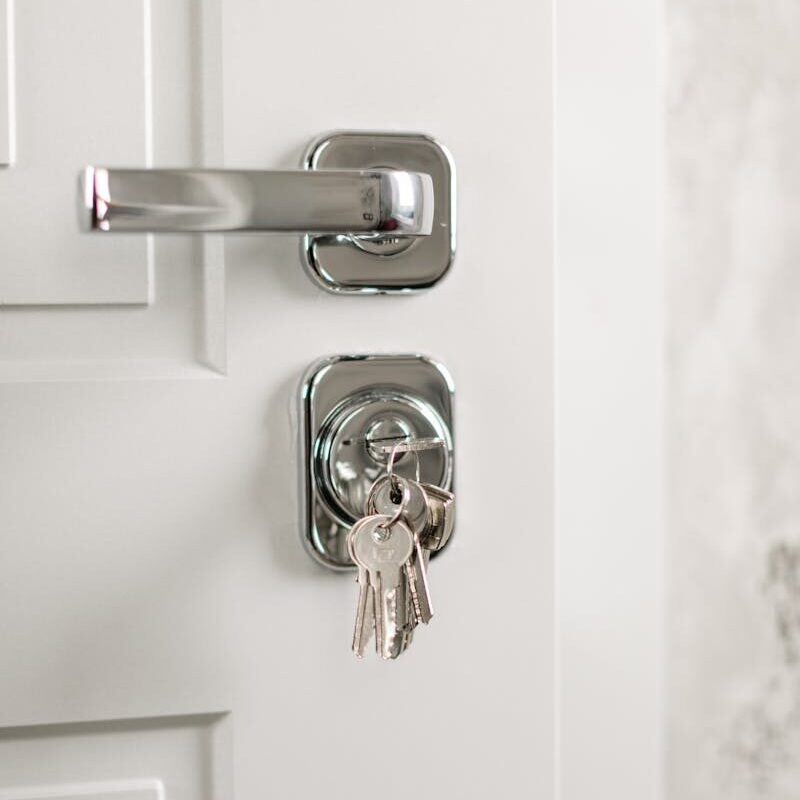 Close-up of a modern silver door handle with keys hanging in the lock, symbolizing security.